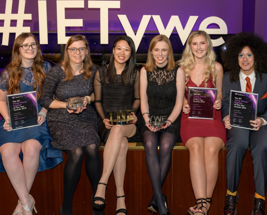 Photograph of six women in eveningwear (some dresses, one suit) holding their metallic awards or framed finalist certificates