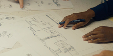 hands pointing at plans printed on a large sheet of paper