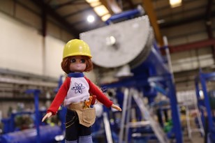 Lottie Tour - doll in hard hat at Star Refrigeration in front of huge blue machinery