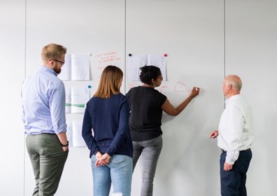 Stock image of four people writing on a whiteboard