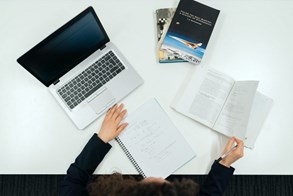 Stock image of a desk with a laptop, notebook, and three books on it