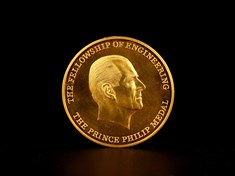 Image of the gold Prince Philip Medal, with an engraving of Prince Philip in profile and text around the edge reading "The Fellowship of Engineering The Prince Philip Medal". Against a black background.