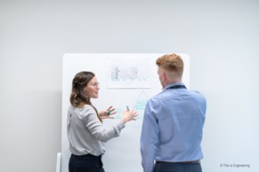 female and male engineers stand discussing at a whiteboard